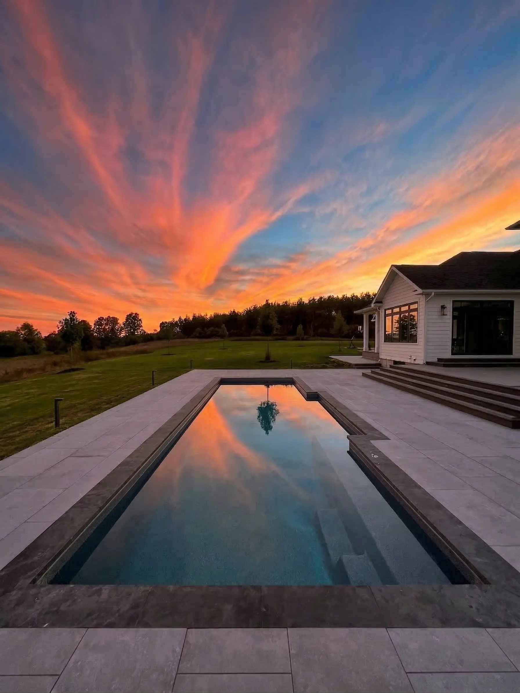 Backyard pool at sunset with farmhouse